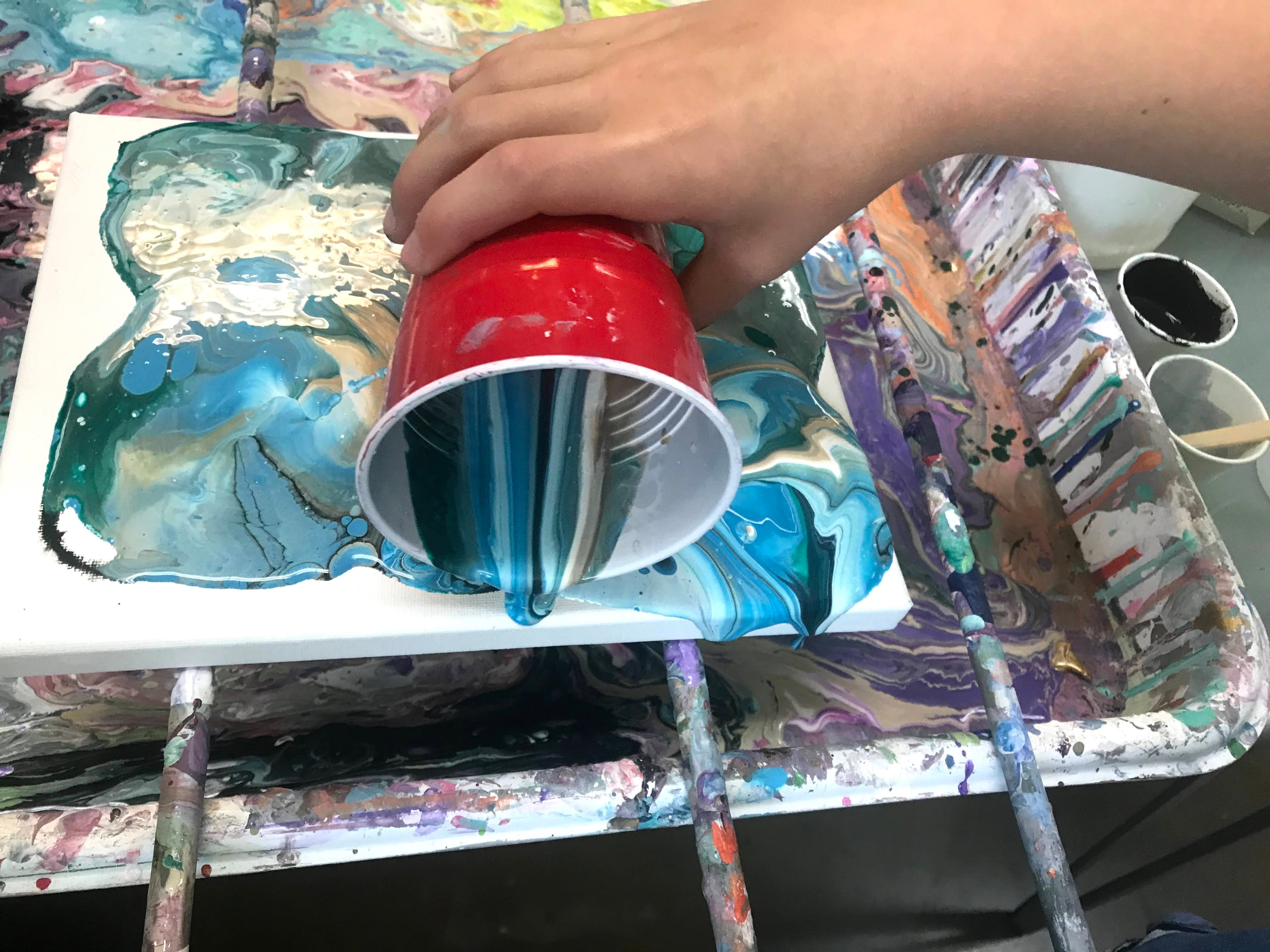 Hands lifting a red cup during a fluid pour painting